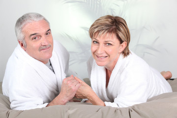 Couple de seniors allongés en peignoir dans un lit