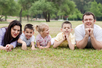 Fototapeta premium Cheerful family of five lying on lawn in the green park
