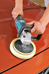 Worker waxing orange car by polishing machine