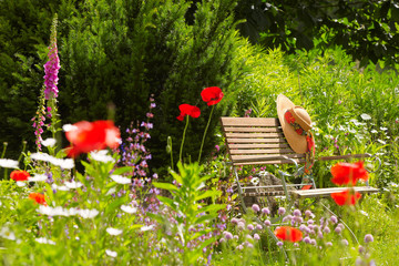 Fototapeta premium garden bench with straw hat within summer flowers 01