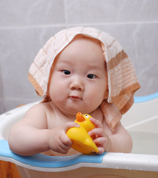 Asian baby boy holding a yellow plastic duck in bath