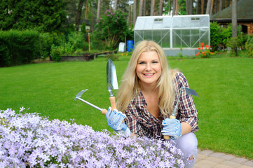 Pretty woman with gardening tools outdoors near flower hill
