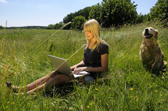 Junge Frau mit Laptop und Hund auf einer Wiese