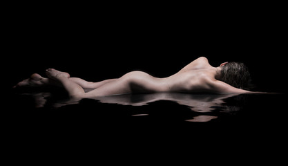 Naklejka premium Nude woman lies in water, low key