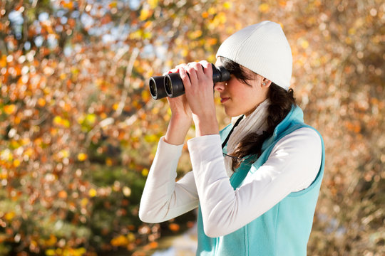 young woman using binoculars in autumn forest