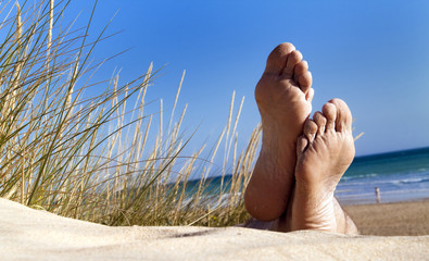 Men's feet lie relaxed in a dune on the beach - obrazy, fototapety, plakaty