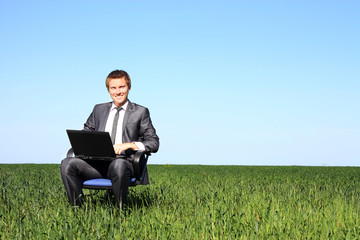 Happy businessman on field, with a laptop