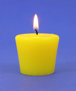 Yellow citronella candle that is lit on a blue background.