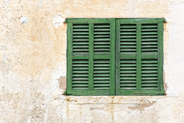 Fototapeta na wymiar Pojedyncze okno z zamkniętymi zielonymi okiennicami na wyblakły elewacji i
