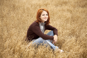 Beautiful red-haired girl at yellow autumn grass.