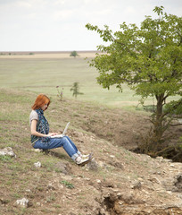 Young beautiful girl with laptop at rock near lake and tree.