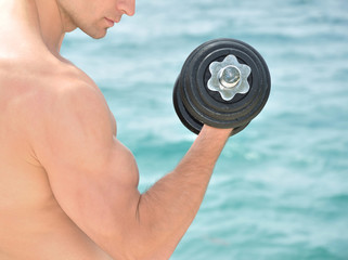 Muscular man lifting weight on the beach