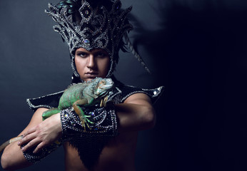 Young pagan priest in ritual suit with green iguana in his hands