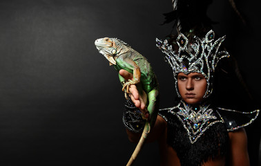 Young pagan priest in ritual suit with green iguana in his hands