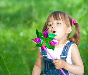 Little girl in jeans blowing on color propeller outdoor