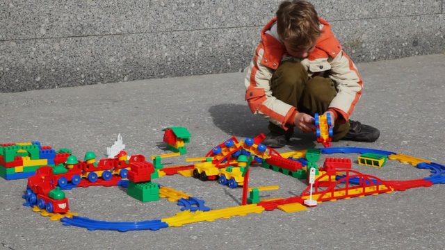 boy collects structure of toy railway in street