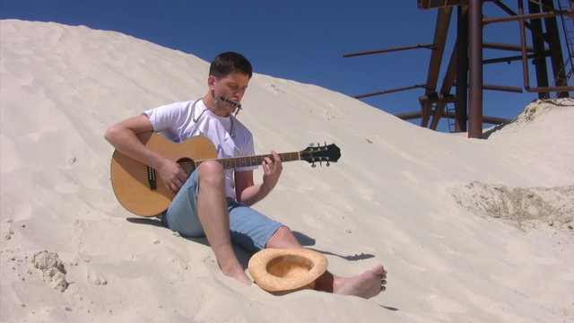 singing man with harmonica plays guitar on beach