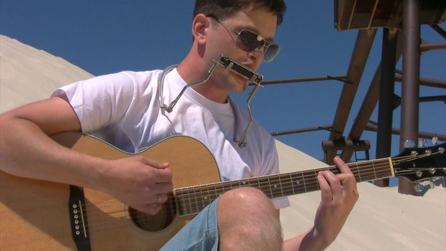 singing man with harmonica plays guitar on beach