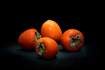 Четыре спелые хурмы на чёрном фоне.