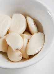 Peeled garlic cloves in white bowl, ready as ingredient.