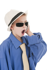A small boy wearing his fathers clothes talking on a phone.