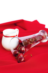 milk jug with a ribbon  glass of cherry  on a red background