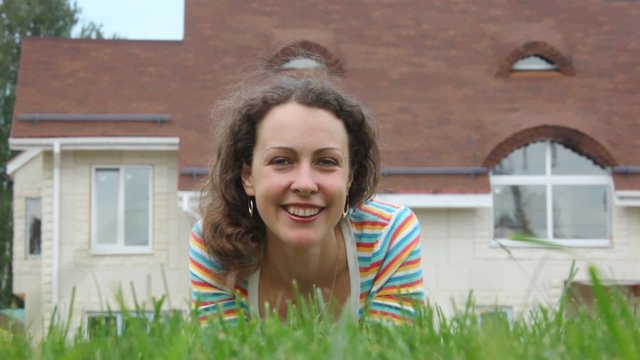 A smiling beautiful woman lays on grass near house