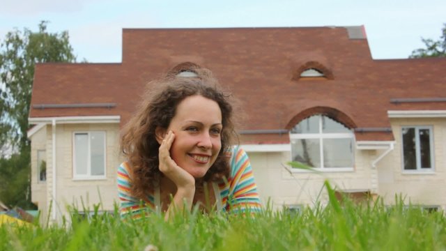 A smiling beautiful woman lays on grass near house