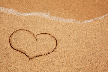 Heart in the sand with wave rolling