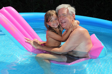 Grandfather and granddaughter cuddling on a lilo in a pool - obrazy, fototapety, plakaty