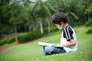 Young boy enjoying his reading book in outdoor park