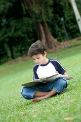 Young boy enjoying his reading book in outdoor park