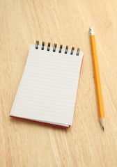 Notepad and yellow pencil on wood background
