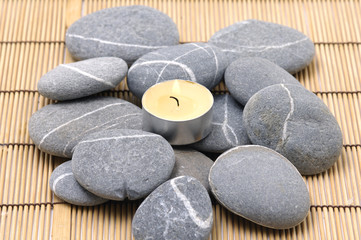 Fototapeta na wymiar A light candle and pebbles on bamboo mat
