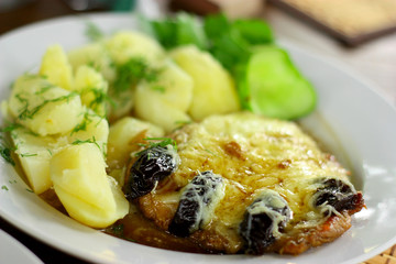Dish with a pork chop and potatoes with dried plums and cheese.