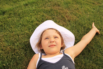 Dziewczynka w białym kapeluszu leży na zielonej trawie