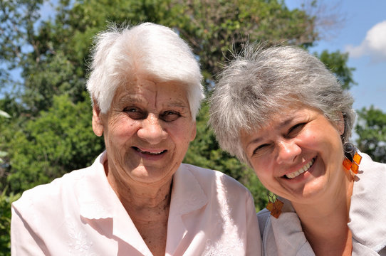 Two elderly women laugh, sitting in nature