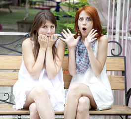 Two girls gossiping on bench at garden.