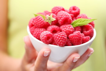 Crockery with raspberries in woman hand.