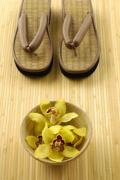 Wooden bowl of orchid with straw flip flops on mat