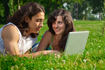 The boy and girl lying on the grass in the park with a laptop
