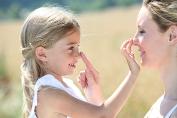 Fototapeta premium Mother and daughter putting sunscreen on their face
