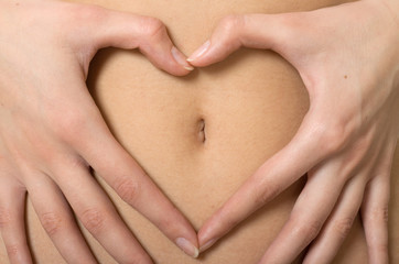 A woman's hands forming a heart symbol around navel