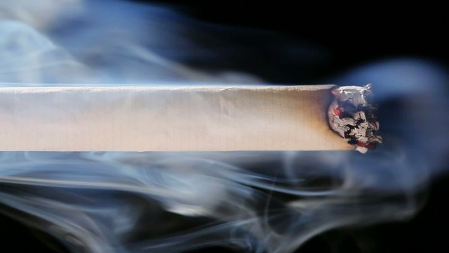 Macro view of burning cigarette with smoke on black