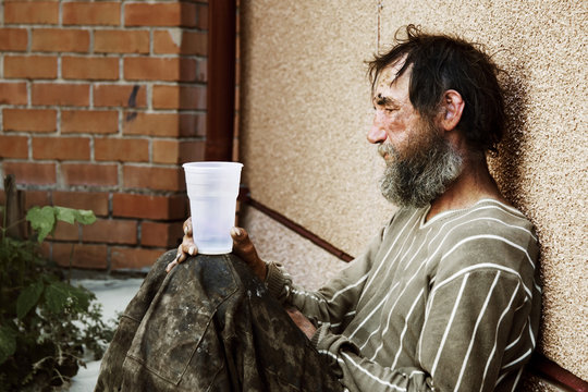Sad homeless man sitting on at the wall on city street