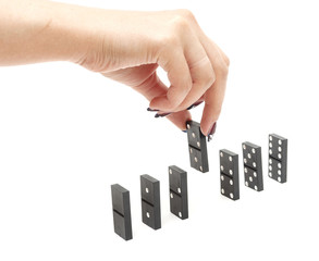 The hand builds a line of dominoes on a black background