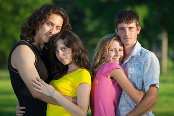 Four young people embrace and stand in the park