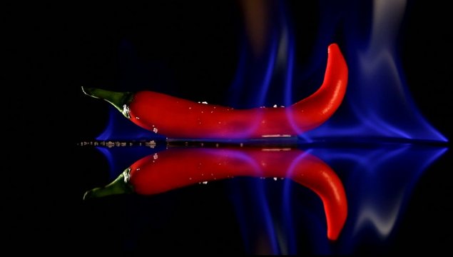 Burning hot Chilli pepper with flame on black mirror background