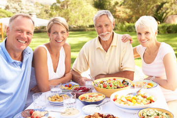 Adult Son And Daughter Enjoying Meal In Garden With Senior Paren