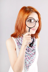 Beautiful red-haired girl with loupe zooming her eye.
